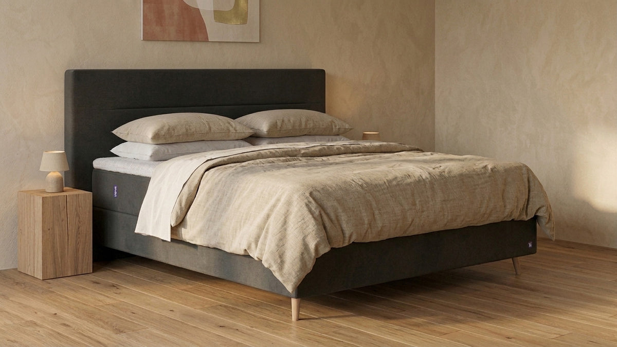 Bruno Boxspringbett mit Linea-Kopfteil, in Anthrazit, Winkelansicht, im Wohnraum, mit Topper, mit Füßen aus nordischer Eiche