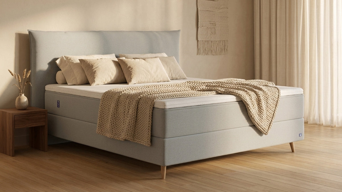 Bruno Boxspringbett mit Pillow-Kopfteil, in Hellgrau, Winkelansicht, im Wohnraum, mit Topper, mit Füßen aus nordischer Eiche